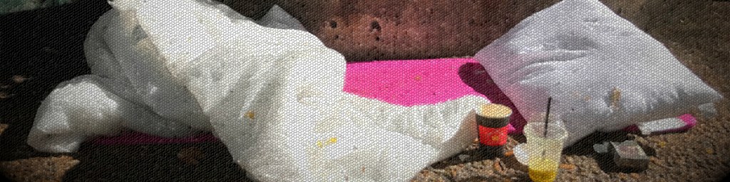 A collection of white pillows and a pink mat lying outdoors, with a couple of cups and food containers beside them.