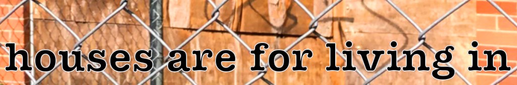 A fence with the phrase 'houses are for living in' displayed prominently in black lettering against a blurred background.