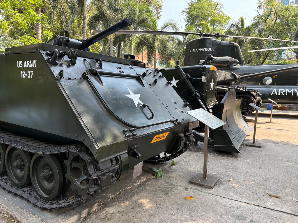 Military display featuring a US Army tank and helicopter, surrounded by greenery.