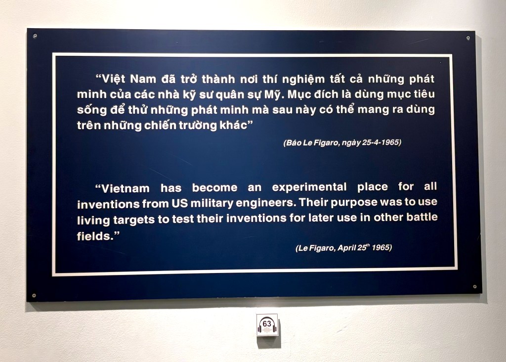 A wall plaque displaying quotes in Vietnamese and English discussing Vietnam as a testing ground for US military inventions during wartime.
