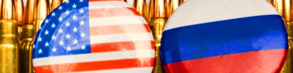 Buttons featuring the flags of the United States and Russia, positioned in front of a background of bullet casings.