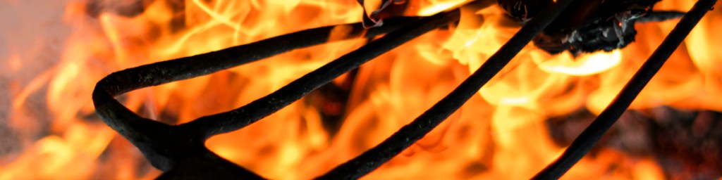 Close-up of a metal pitchfork against a backdrop of bright flames.