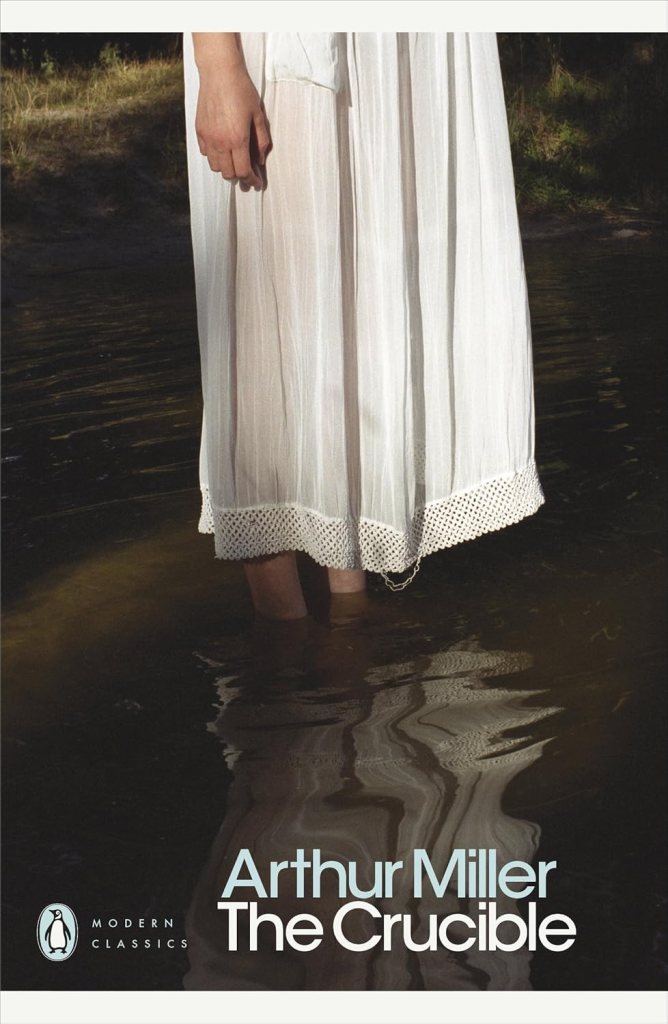 A person standing in shallow water, wearing a long white dress, with reflected light creating subtle ripples in the water, alongside lush greenery in the background. The cover prominently features the title 'The Crucible' by Arthur Miller.