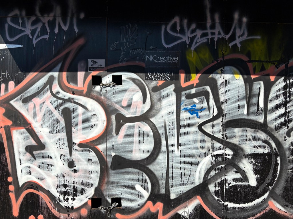 A vibrant piece of urban street art featuring bold graffiti and abstract lettering, predominantly in shades of black, pink, and green.