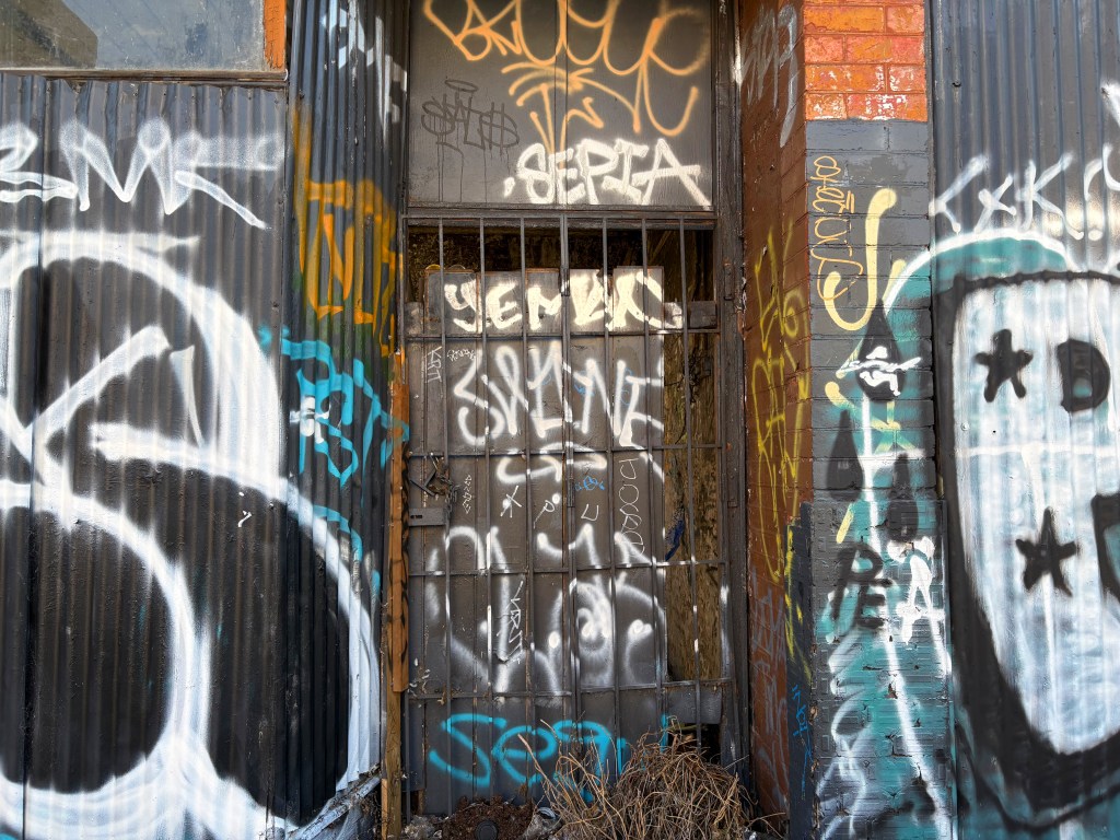 A close-up of a barred door against a background of colourful graffiti on a corrugated metal wall.