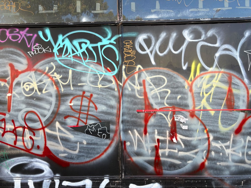 A wall covered in various layers of colourful graffiti, including tags and symbols in red, blue, and black.