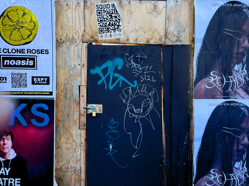 A wooden wall covered with posters for 'The Clone Roses' and other events, featuring graffiti and a locked door with a keyhole.