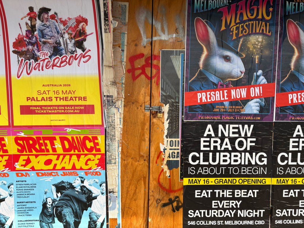 A collage of colourful posters on a wooden wall advertising various events, including a concert by The Waterboys, the Melbourne Magic Festival, and a street dance exchange, with details on dates and locations.