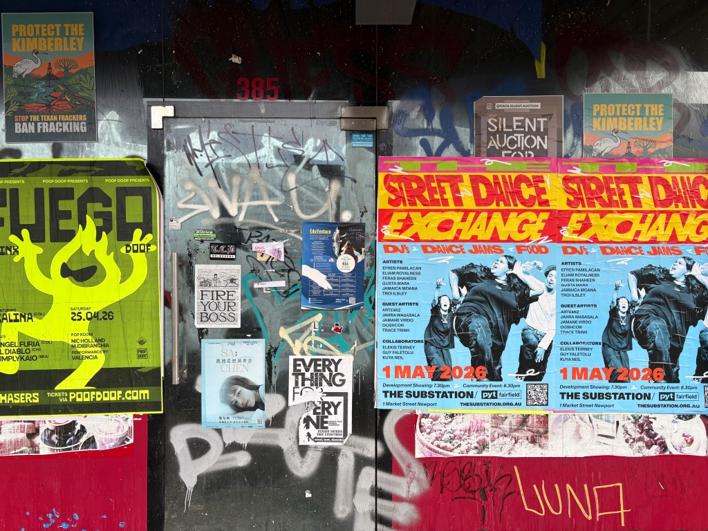 A collage of vibrant posters on a wall, featuring advertisements for events including a dance exchange, a fight against fracking, and various artistic performances. The wall is covered in graffiti and has a door marked with the number 385.