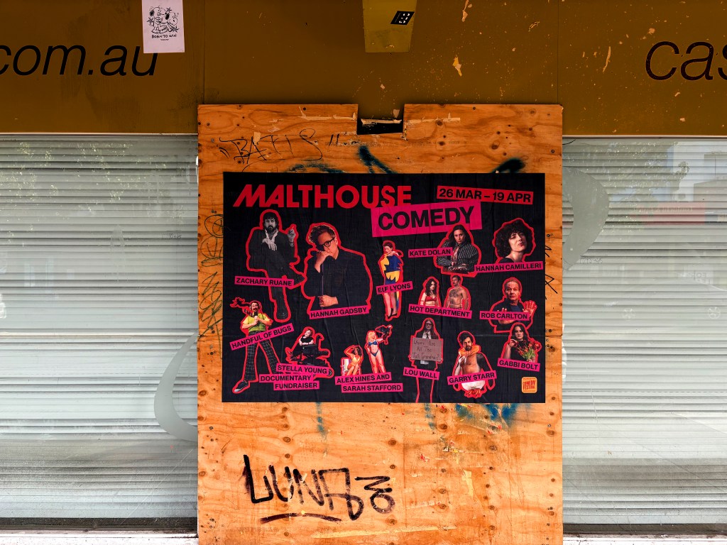 Poster advertising Malthouse Comedy event featuring various performers from 26 March to 19 April, displayed on a wooden board.