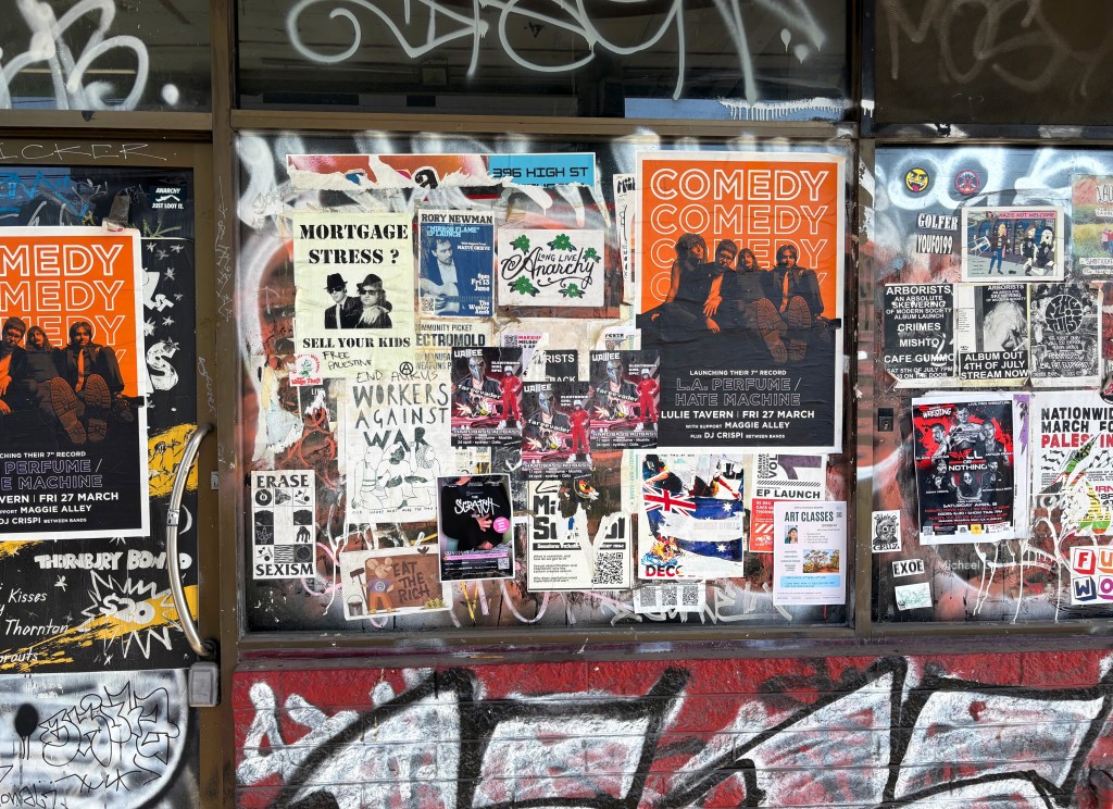 A collection of posters and flyers displayed on a window, promoting events such as a comedy show and art classes, surrounded by graffiti.