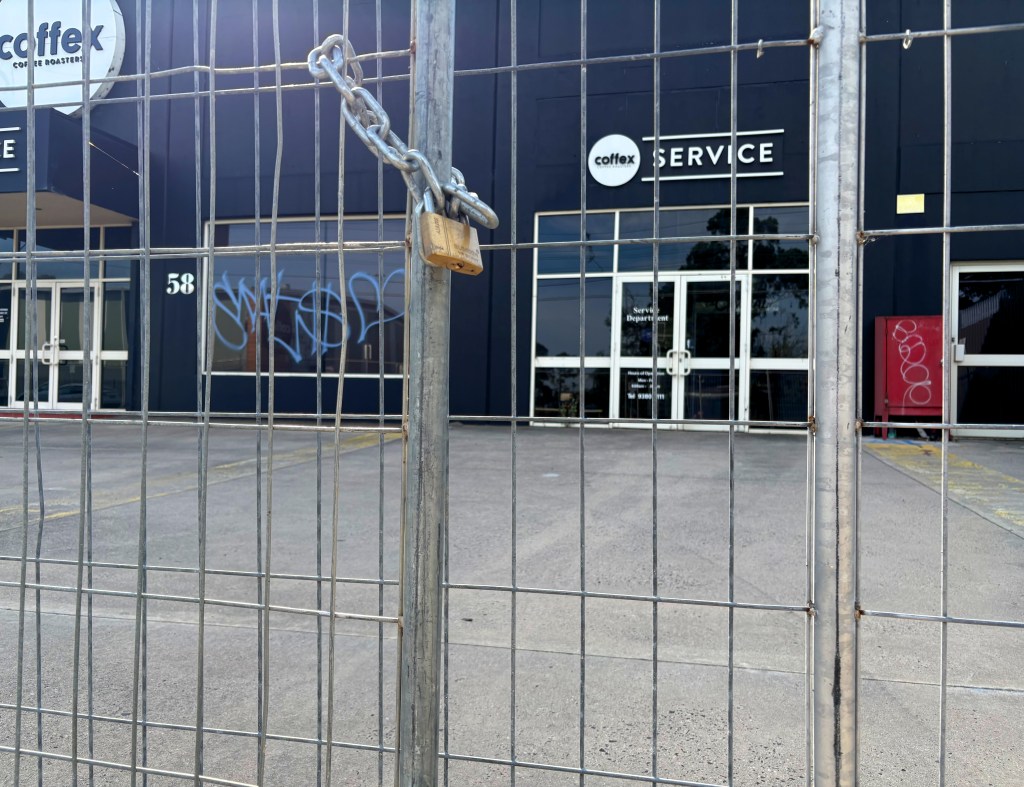 A locked chain link gate in front of a building with the word 'SERVICE' displayed and graffiti on the window, located at number 58.