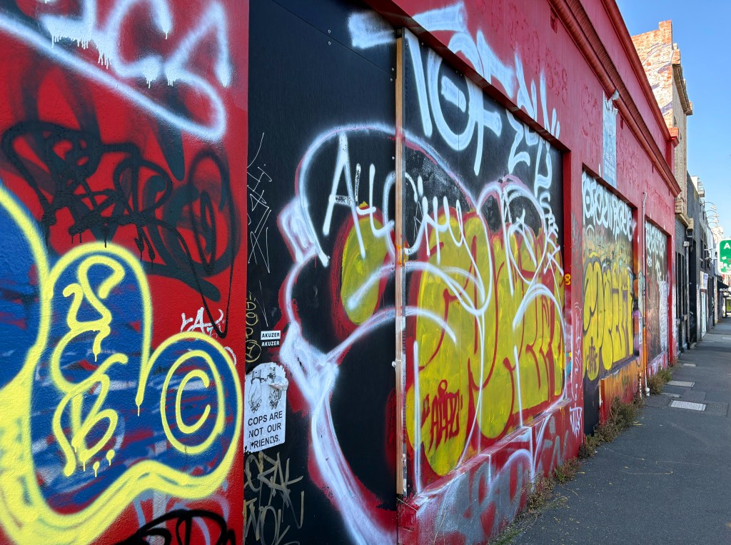 A vibrant wall covered in various graffiti art, featuring bright colours like red, yellow, and blue, with stylised tags and a prominent sticker reading 'COPS ARE NOT OUR FRIENDS.'