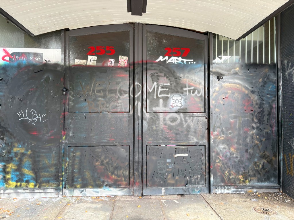 Graffiti-covered shopfront doors numbered 255 and 257, with various stickers and a message reading 'WELCOME to...' partially visible.