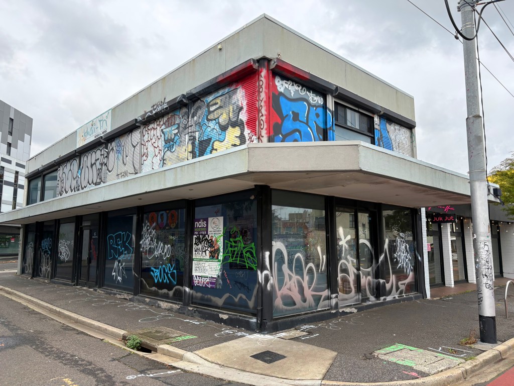 A corner building covered in graffiti, featuring a mix of vibrant colours and designs, with large windows and a flat roof.