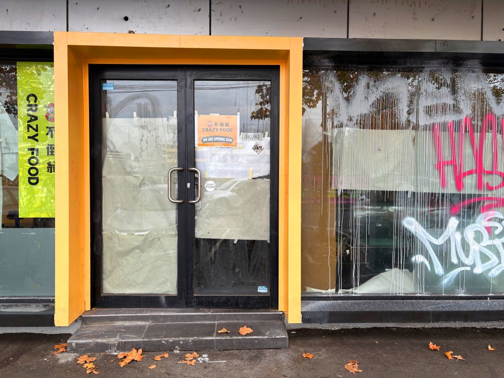 Exterior view of a closed restaurant with the name 'Crazy Food' on the door, featuring a bright orange frame and graffiti on the windows.