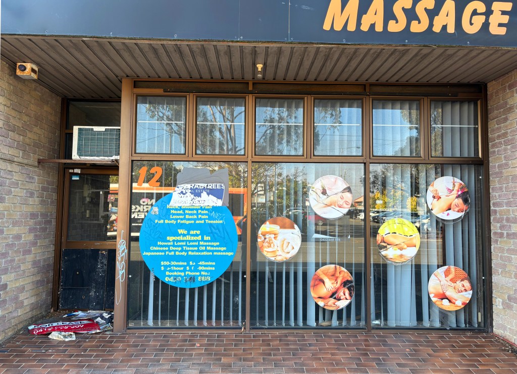 Exterior view of a massage therapy centre featuring a sign with the word 'Massage' and a list of services offered, including various types of massages. The windows display circular images of people enjoying massages.