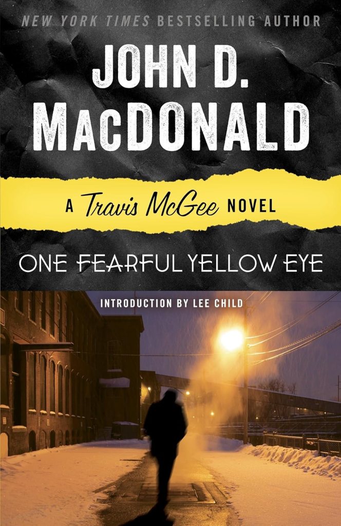 Book cover of 'One Fearful Yellow Eye' by John D. MacDonald, featuring a shadowy figure walking in a snowy urban setting with street lighting.