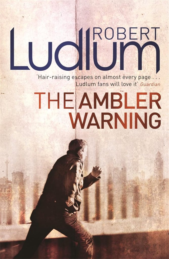 Book cover of 'The Ambler Warning' by Robert Ludlum, featuring a man in a jacket looking out at a cityscape.