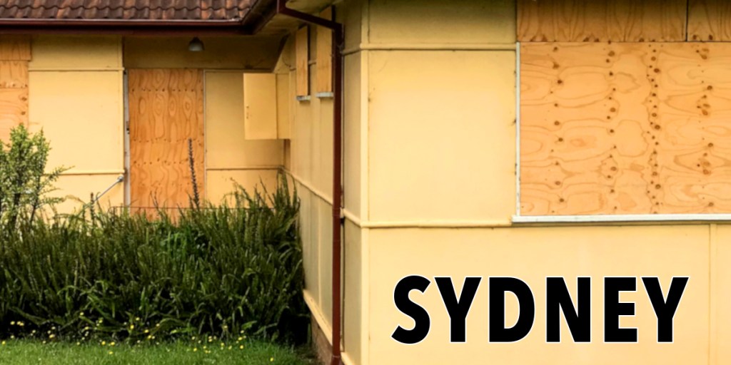 A partially boarded-up house with yellow walls and a garden in front, featuring the text 'SYDNEY' prominently displayed.