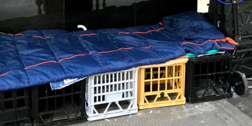 A makeshift bed created using plastic crates and a sleeping bag, situated in a vehicle.