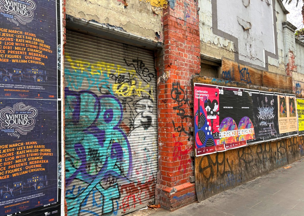 A wall covered with various posters and vibrant graffiti, including advertisements for events like 'Winter Sounds' and 'Castlemaine Documentary Festival'.