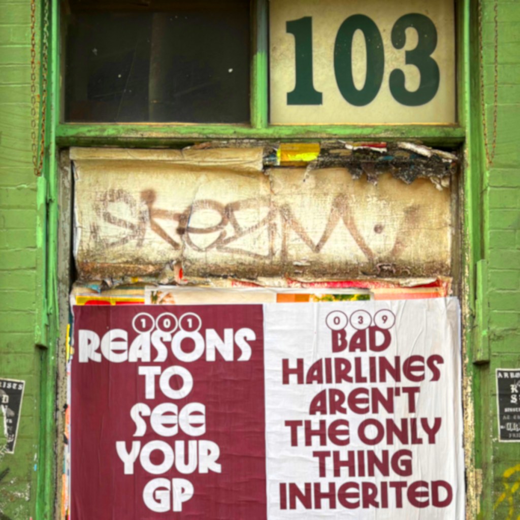 A weathered door with the number 103 displayed above, partially obscured by a large banner reading '101 REASONS TO SEE YOUR GP' on the left and '039 BAD HAIRLINES AREN'T THE ONLY THING INHERITED' on the right, against a green wall.