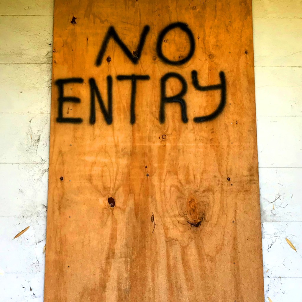 A plywood panel with the phrase 'NO ENTRY' spray-painted in black.