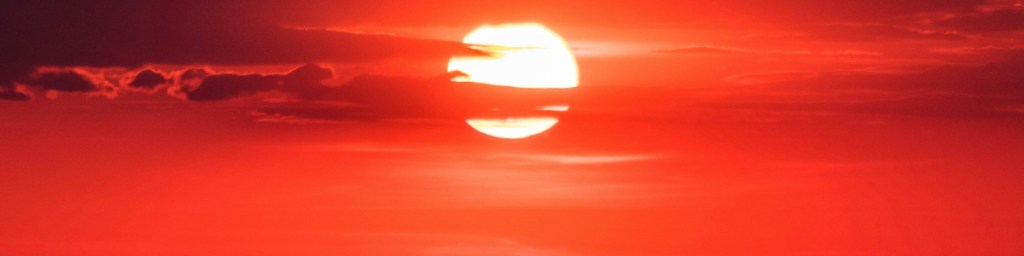 A vibrant sunset with a large sun surrounded by reddish-orange sky and clouds.